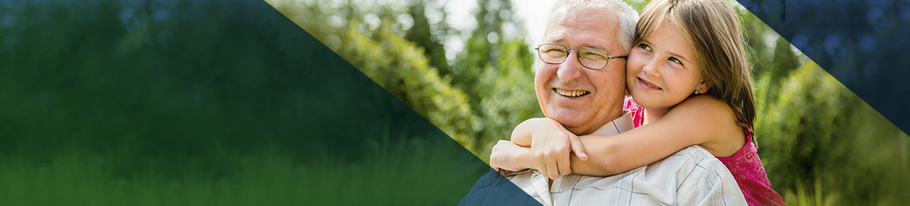 Smiling grandfather with glasses as his young, smiling granddaughter hugs him tightly around his shoulders from behind