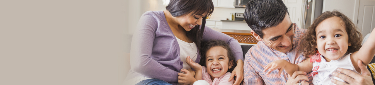 Young family with a mom and dad laughing on couch with their two little girls