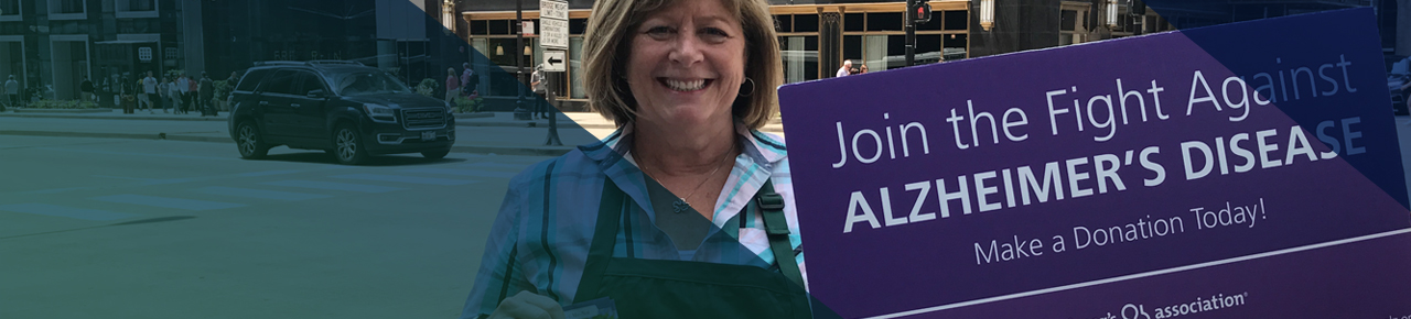 Smiling woman wearing an apron and holding purple sign about fighting Alzheimer’s Disease