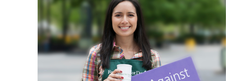 Smiling woman wearing an apron and holding purple sign about fighting Alzheimer’s Disease